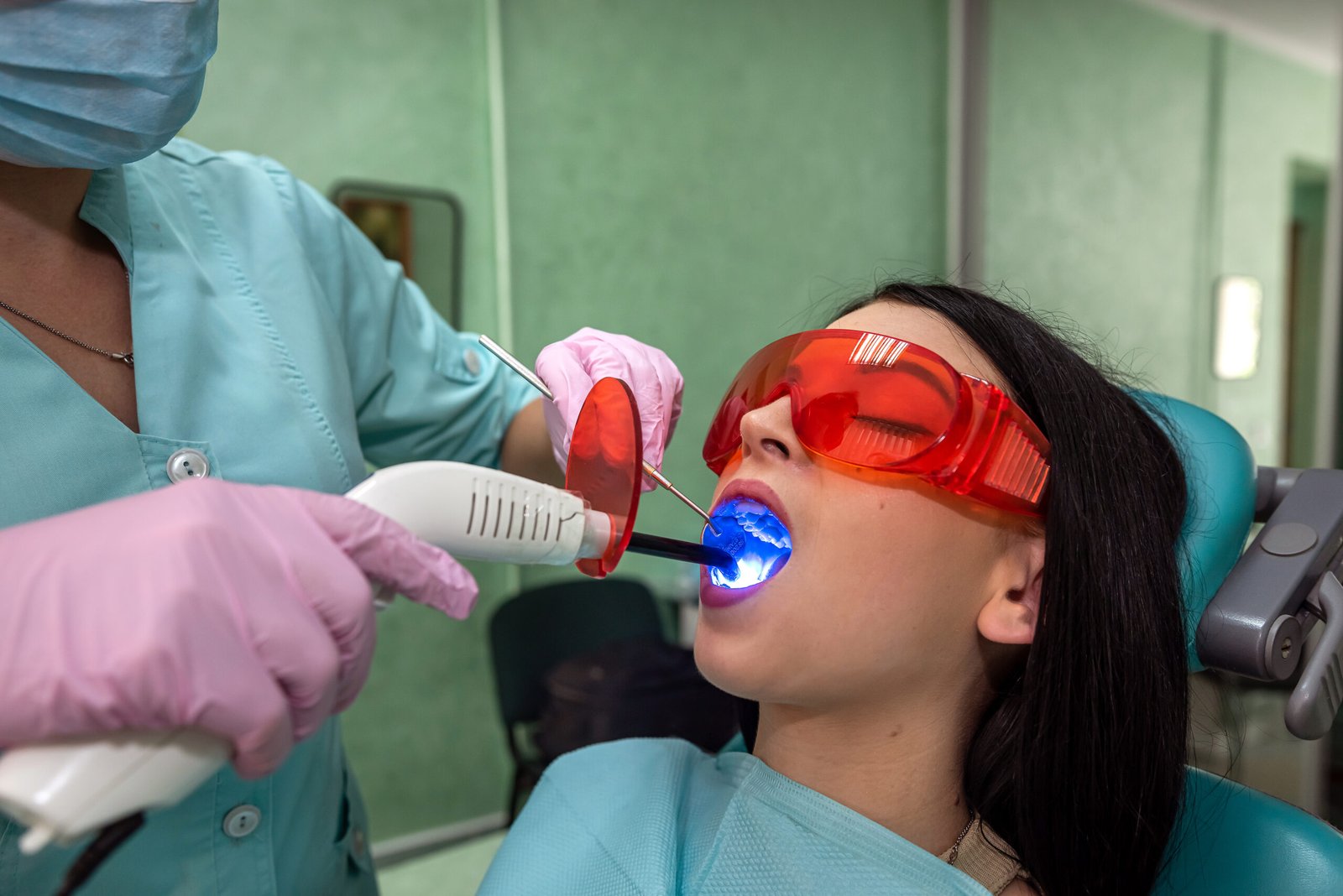 Patient with open mouth sitting in dentist chair in protective glasses.