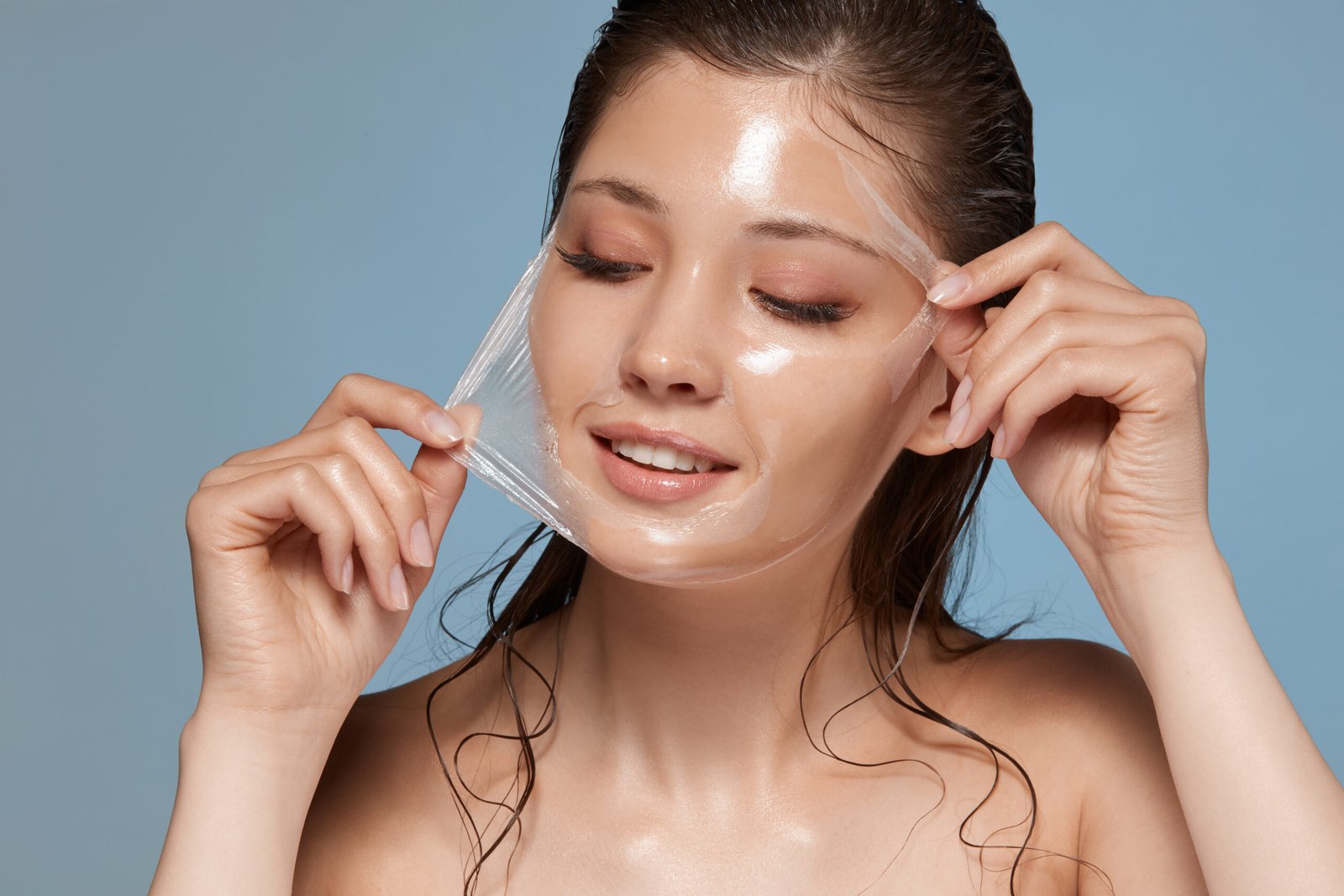 young and happy woman removes facial mask and looking down to the side, female skin care, copy space, cosmetology treatment