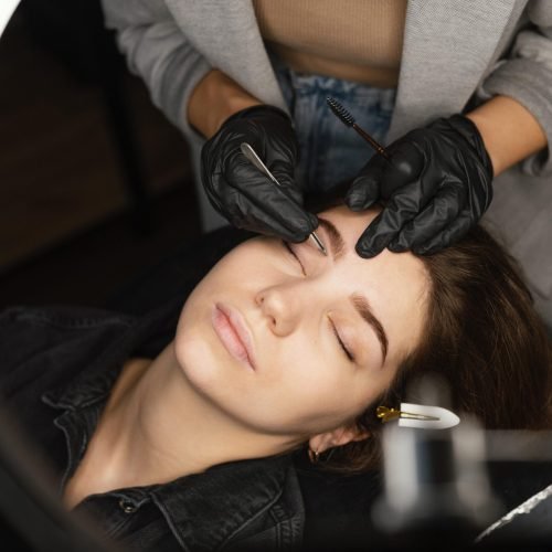 top-view-female-clinician-doing-eyebrow-treatment-woman